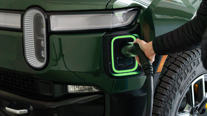 person charging electric vehicle with rivian ev charging connector