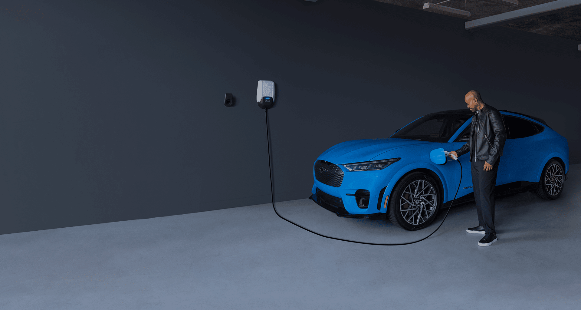 man charging blue EV in gray garage