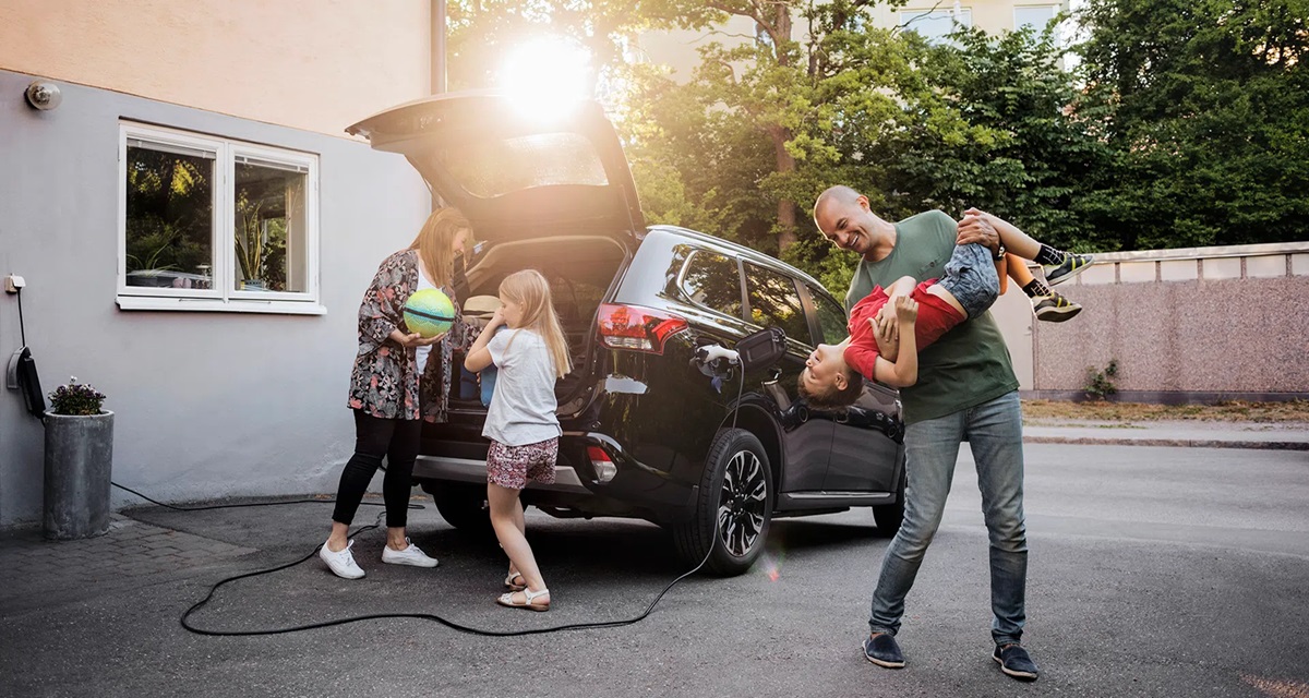 Happy family charging EV outside home.
