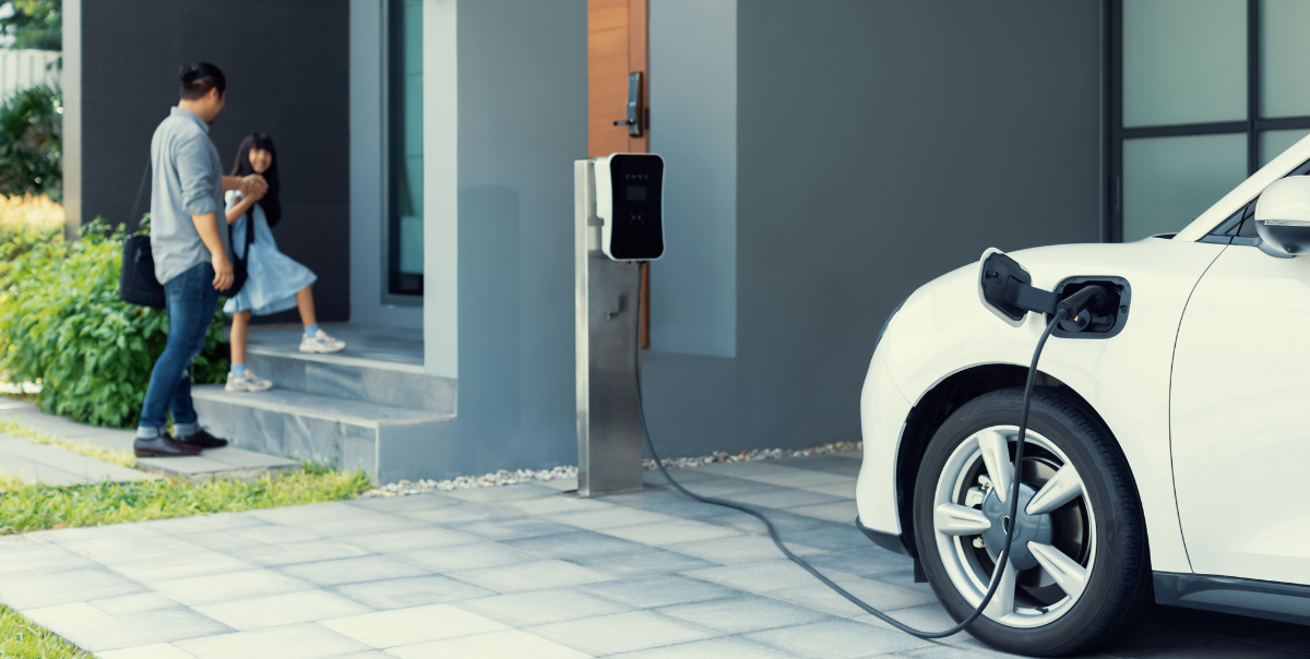 A father and daughter entering a home, where an electric vehicle charges outside, underscoring the importance of incorporating EV battery charging best practices to ensure the lasting health of your car's battery