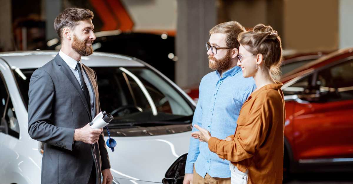 image depicts young couple speaking with auto sales manager to purchase an electric vehicle as the inflation reduction act evolved for evs to increase savings and boost ev adoption