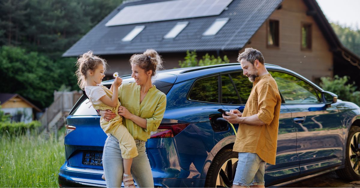 Happy family standing next to their charging EV outside their home equipped with solar panels, highlighting the synergy between battery storage and solar energy integration