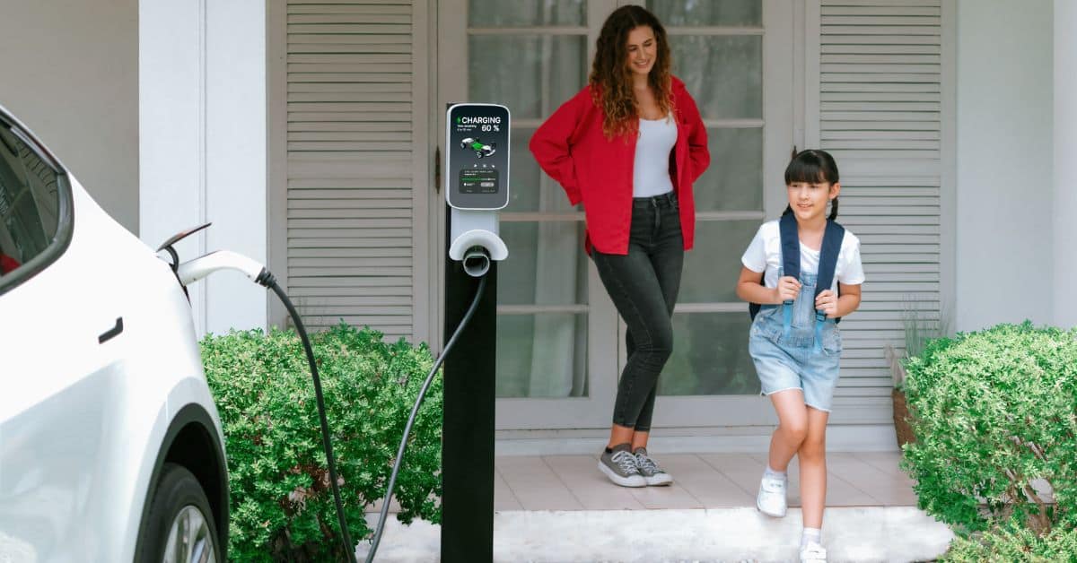 A happy young girl and her mother walking towards their EV, which is being charged with a home charger, highlighting how a professionally installed EV charger can enhance convenience and increase home value