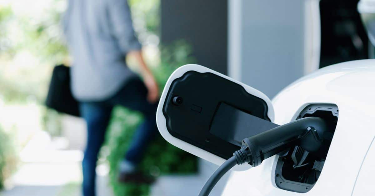An electric car at a home charging station with a blurred figure walking behind, symbolizing the convenience of personal charging solutions for plug-in hybrid vehicle owners
