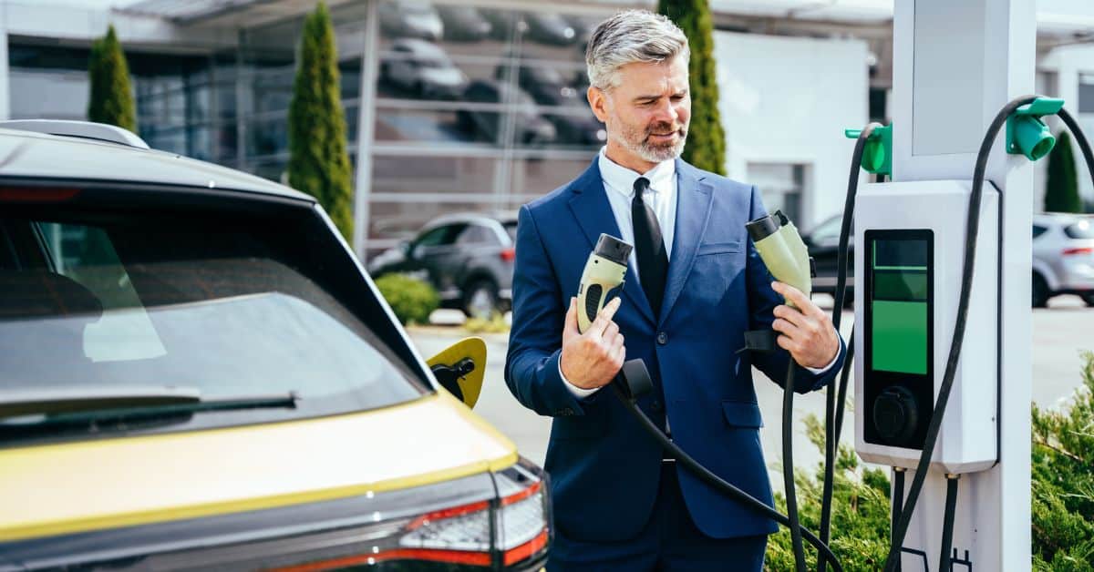 A man thoughtfully examining two different plug-in cables at an outdoor EV charger, illustrating the evolving landscape and the importance of understanding EV charging standards for consumers