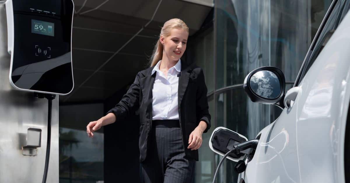 A businesswoman in a suit approaching an electric car charging at a workplace station, showcasing the practicality and integration of business EV chargers