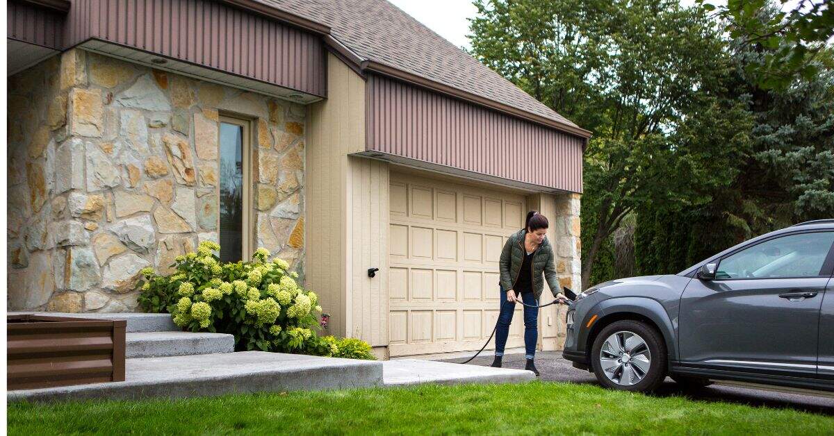A woman charging her electric vehicle outside her home, highlighting the diverse factors that play a role in determining the cost of electric vehicle charger installation
