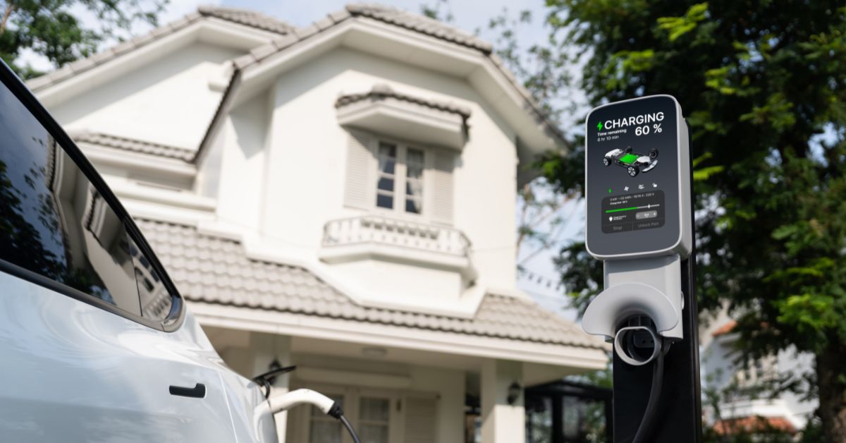 An electric vehicle linked to an EV charger in front of a house, representing the significance of electric vehicle fleet charging infrastructure driving sustainability initiatives forward