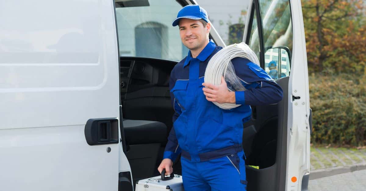 A smiling electrical contractor stands beside a van, equipped with a toolbox and cables, embodying preparedness for EV charging business opportunities
