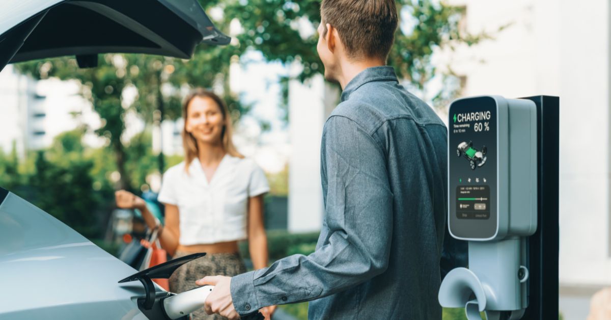 A young couple chatting next to an electric vehicle being charged, showcasing the practicality and relevance of a commercial electric vehicle charging station