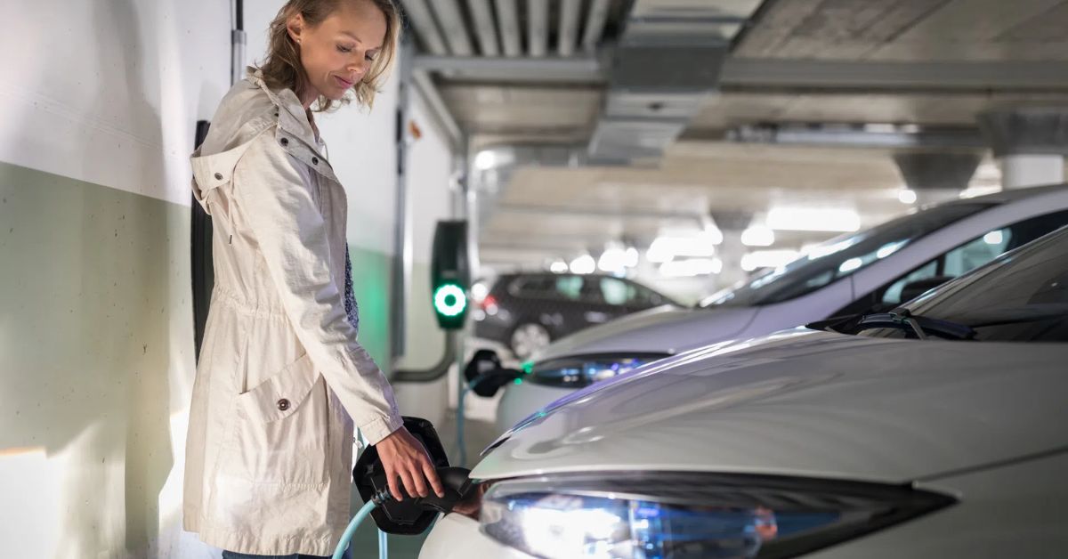 Inside a multifamily building garage, a woman charges her EV, illustrating the practicality of EV charging stations for multifamily residences